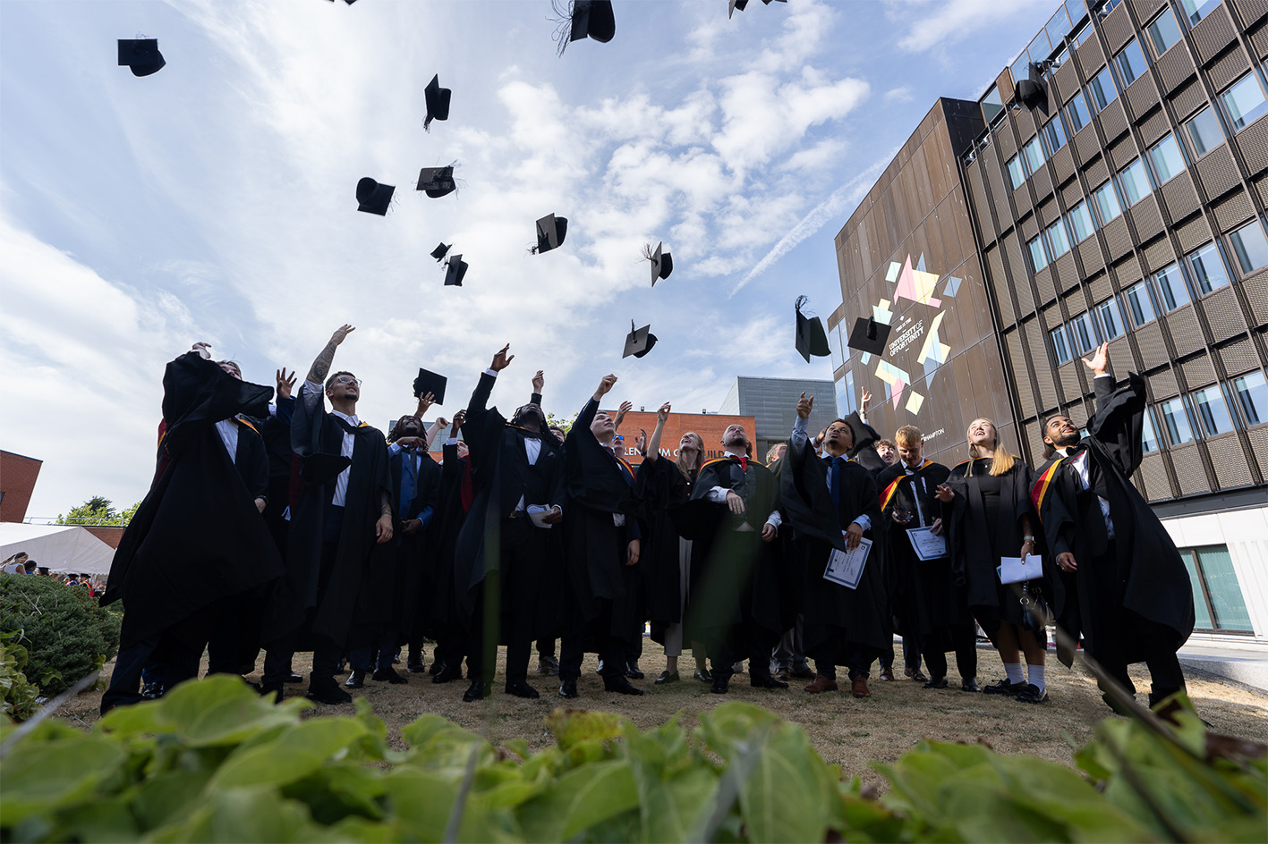 Football Coaching and Performance cohort throwing graduation caps in the courtyard