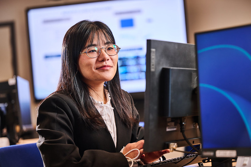 A smiling female student sits at a desktop computer in a computer lap