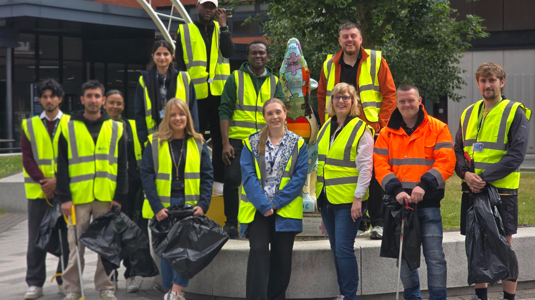 A group of staff and student volunteers wearing high vis' vests holding bin bags and litter pickers in the City Campus Courtyard for a community litter pick activity