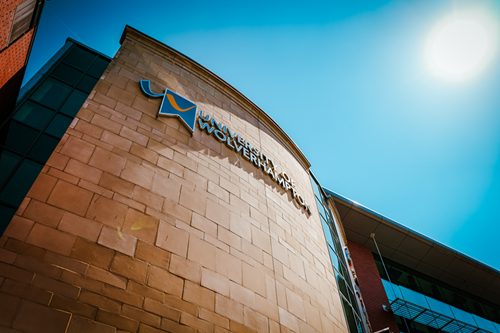 Photo of a university building taken from below, showing the university logo and blue skies above