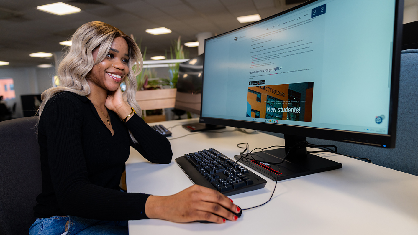Smiling female student on a PC in the library visiting the University website