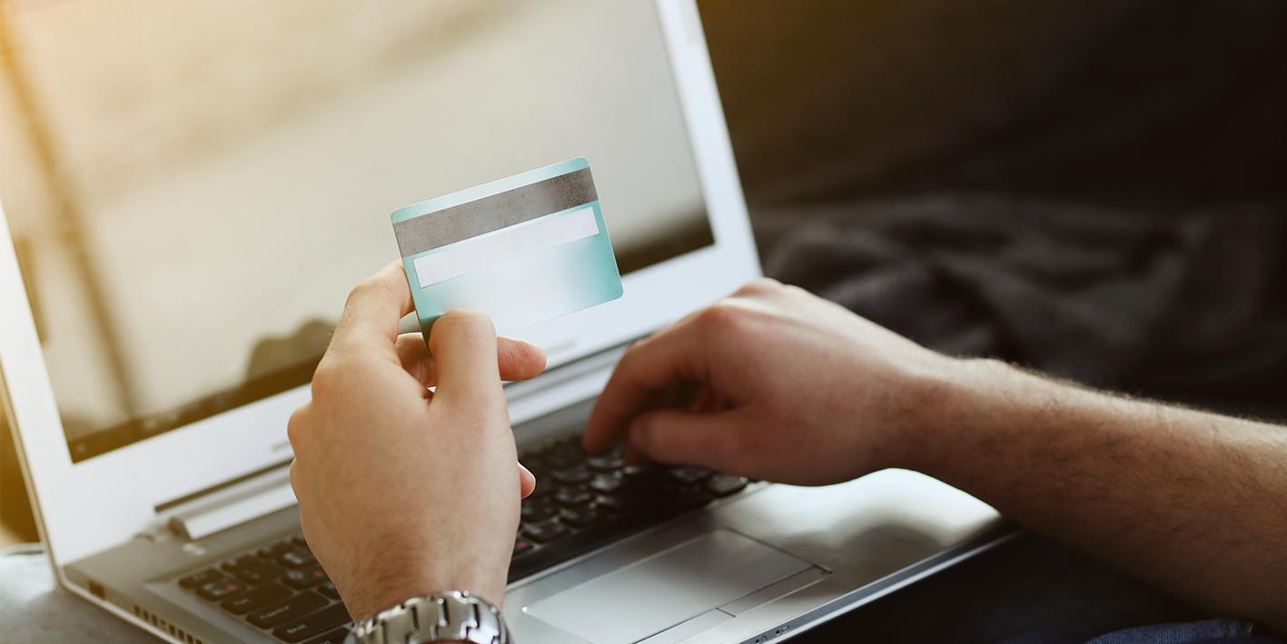 person at laptop holding payment card about to make an online payment