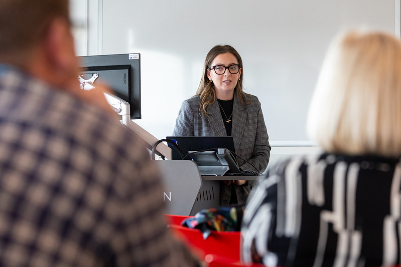 A presenter stands in front of audience in a class room