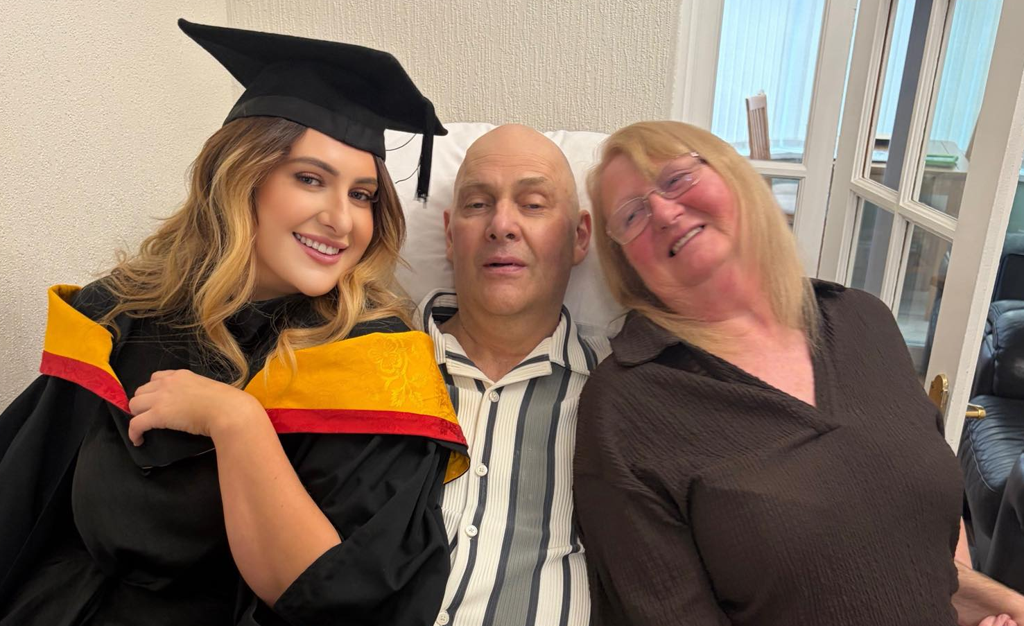 Danielle Keay sits with her father, Dave and mother, Lorraine wearing her graduation gown and mortarboard.