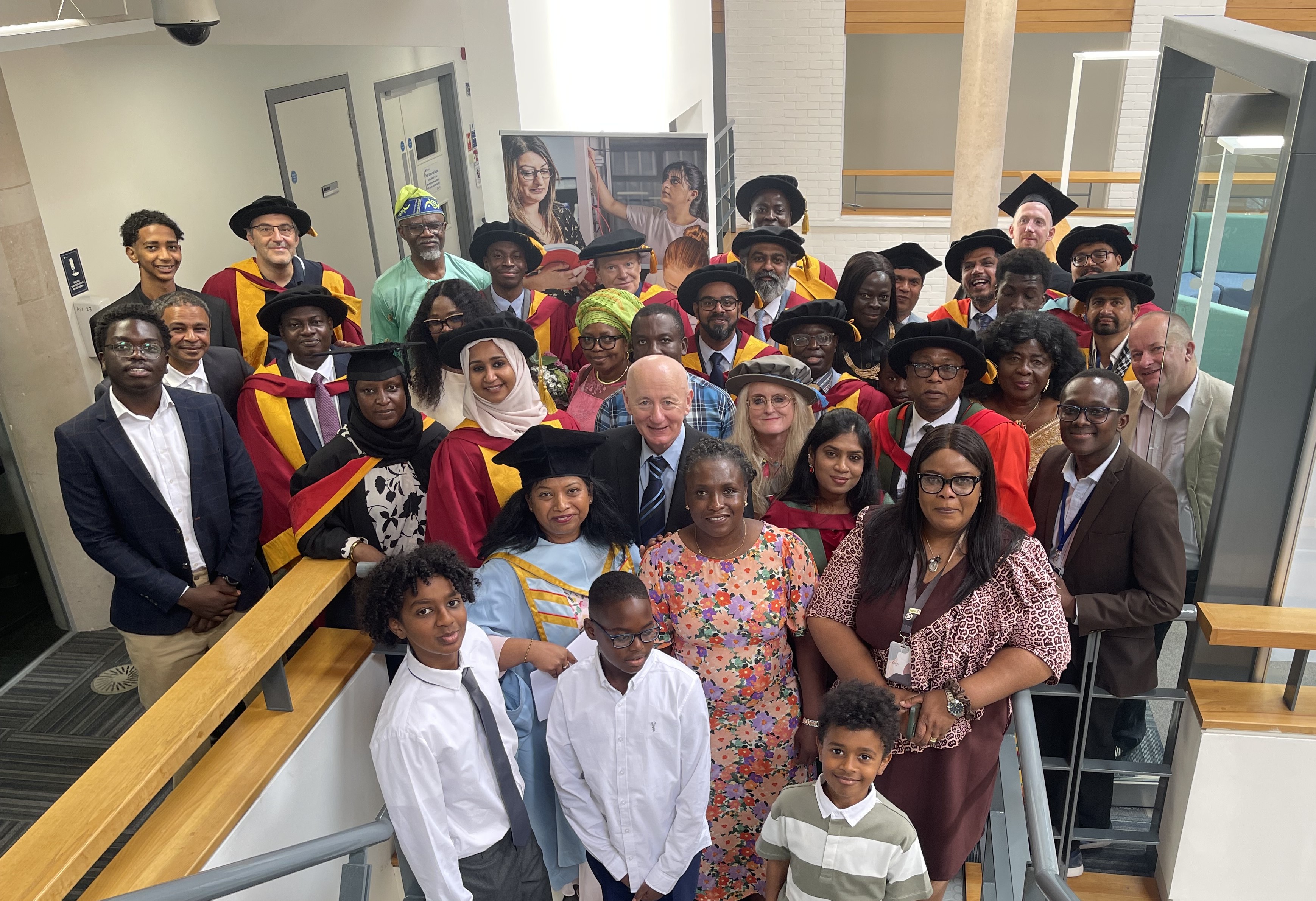 Members of staff, students and their families from the university’s Faculty of Science and Engineering gather for a photograph. they are gathered at the foot of some stairs on graduation day. Graduates and academics don graduation gowns and hats of different, vibrant colours