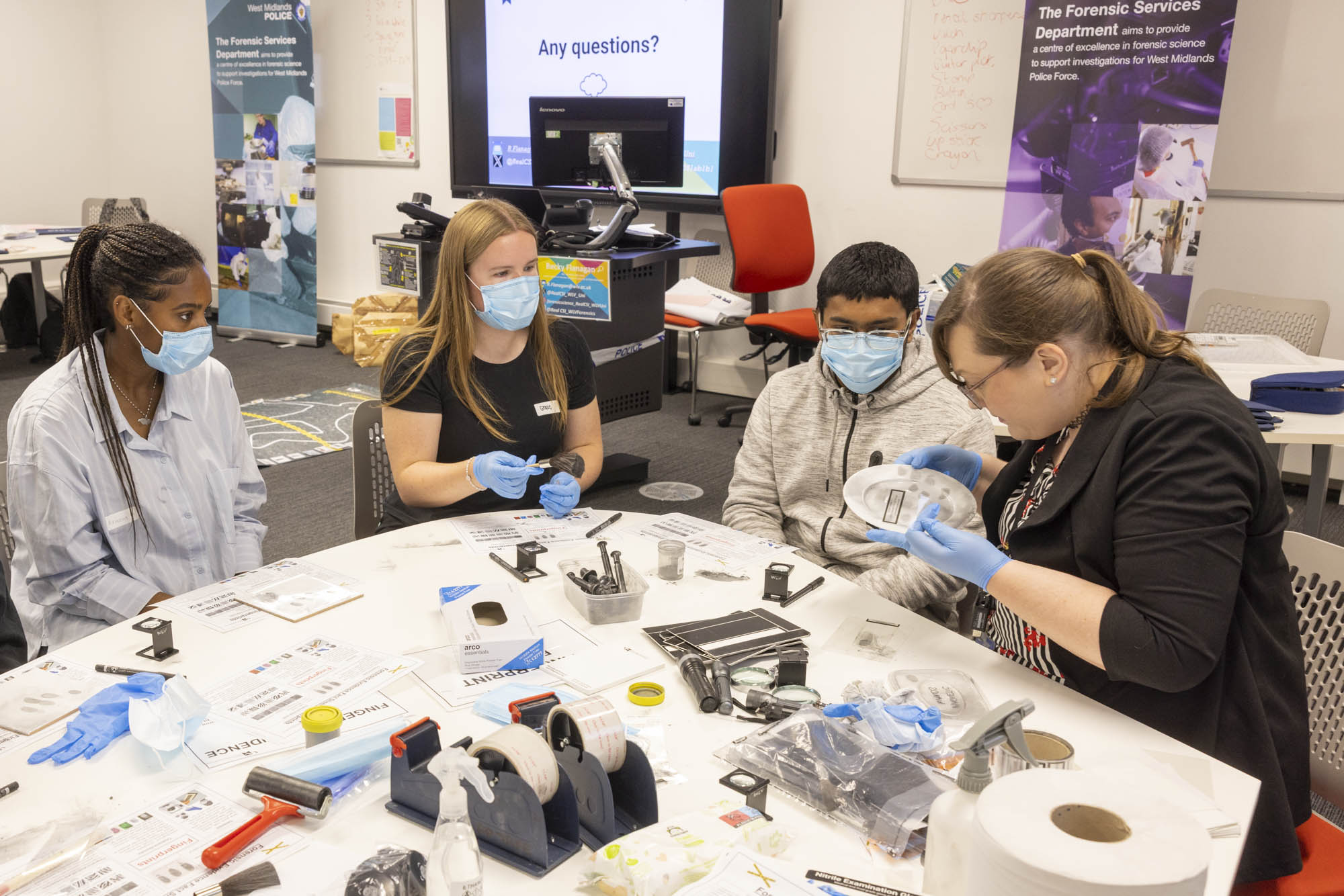 Three students are sitting around a table, learning to assess fingerprints from a crime scene