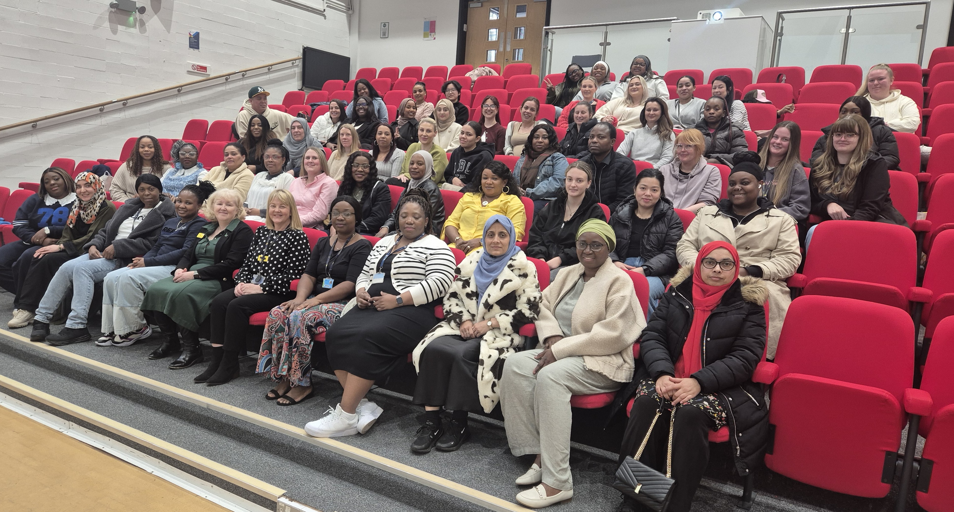 Over twenty final-year nursing students are seated in a lecture theatre. They are dressed casually and look towards the camera for a group photo