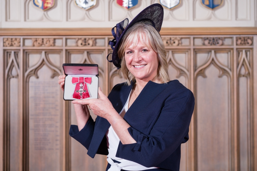 Prof. Arkell shows off her MBE at Windsor Castle. She is smartly dressed in a navy blue suit with matching hat.
