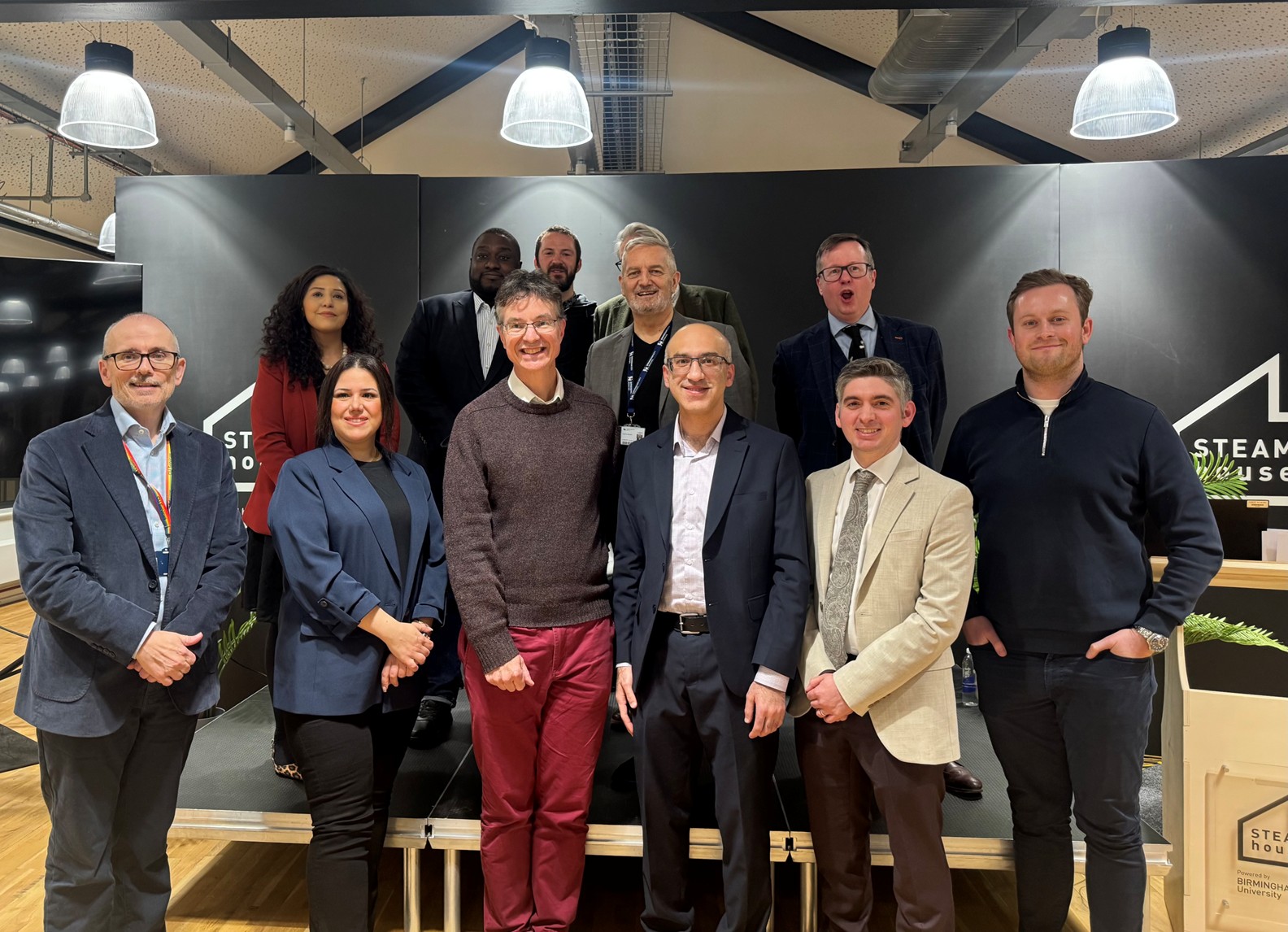 Representatives from West Midlands universities and businesses stand in two rows for a picture at the business event