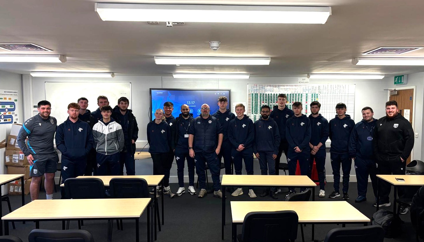 Twenty students and lecturers from the University of Wolverhampton line up for a photograph at the front of a classroom at West Bromwich Albion