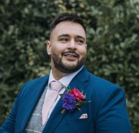 Photograph of Dave Anson outdoors in front of a hedge, wearing a blue suit.