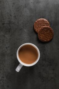 A vertical view of a cup of tea and two chocolate digestives