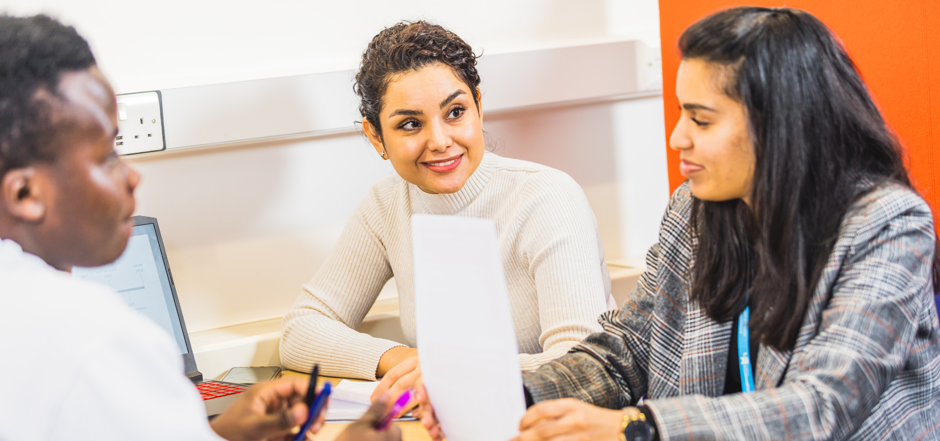 Three people sitting at a table, in conversation and reading from documents