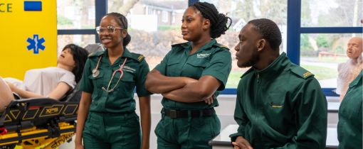 Paramedic Science students standing with uniform on listening to lecturer with dummy next to them