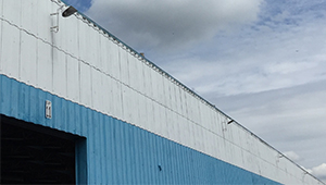 A photograph of a metal industrial building painted in two contrasting shades of blue, pictured against a blue sky
