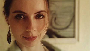 Photograph of Helen Calcutt looking into the camera in front of a framed piece of art