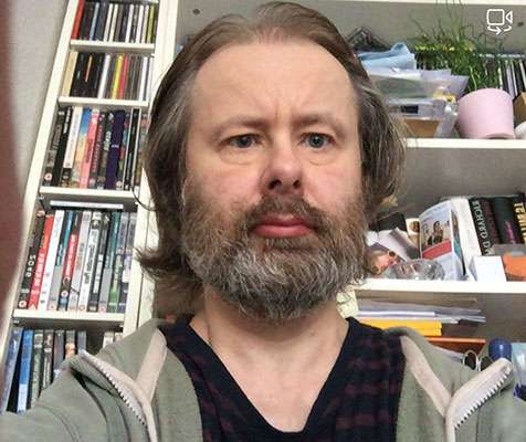 Julian Gwinnett, DSN Co-chair, photographed from a webcam in front of a set of shelves.
