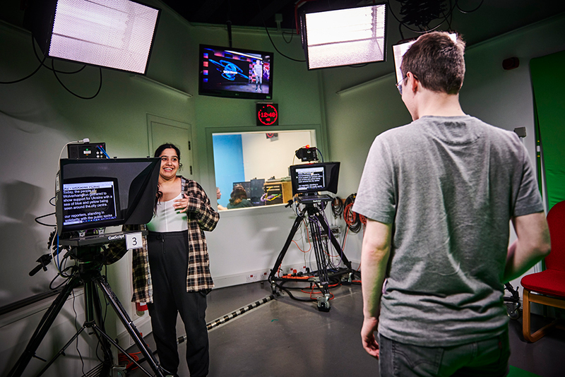 2 students, one male one female, recording a TV newslot in the TV studio in the screen school