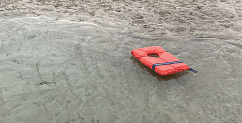 Photograph of a life jacket, washed ashore on an empty beach