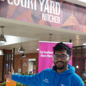 A student ambassador in a labelled blue hoodie gesturing towards the Courtyard Kitchen