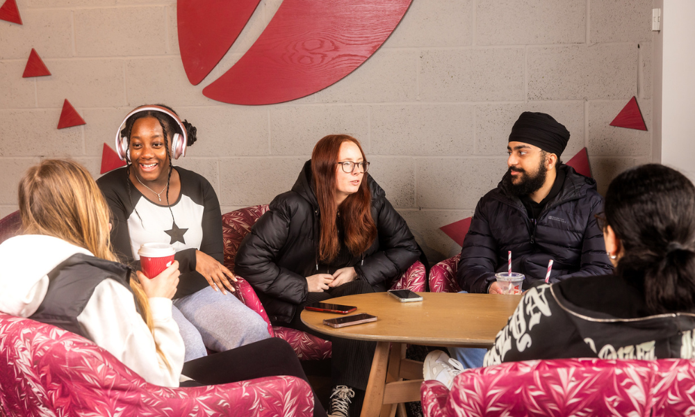 A group of students around a table in Costa Coffee, holding coffee cups with their phones on the table