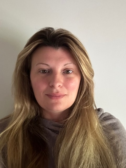 Photograph of Donna-Louise Harvey wearing grey against a white wall.