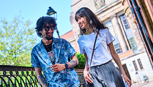 Two students walking along a footpath away from the University entrance