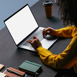 Person sat at desk using laptop with notebook next to them.