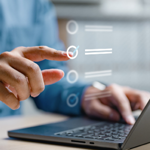 Hand pointed to a checked off box on a to do list, while using a laptop at a desk.