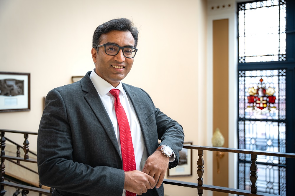 Professor Prashant Pillai, Pro-Vice-Chancellor Research and Knowledge Exchange, standing against a banister at the top of a staircase in front of a window with a stained glass design.