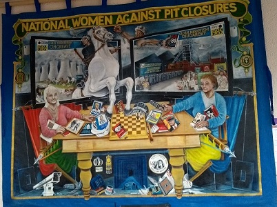A large banner with 'National Women Against Pit Closures' at the top, depicts scenes from recent mining histroy including Orgreave