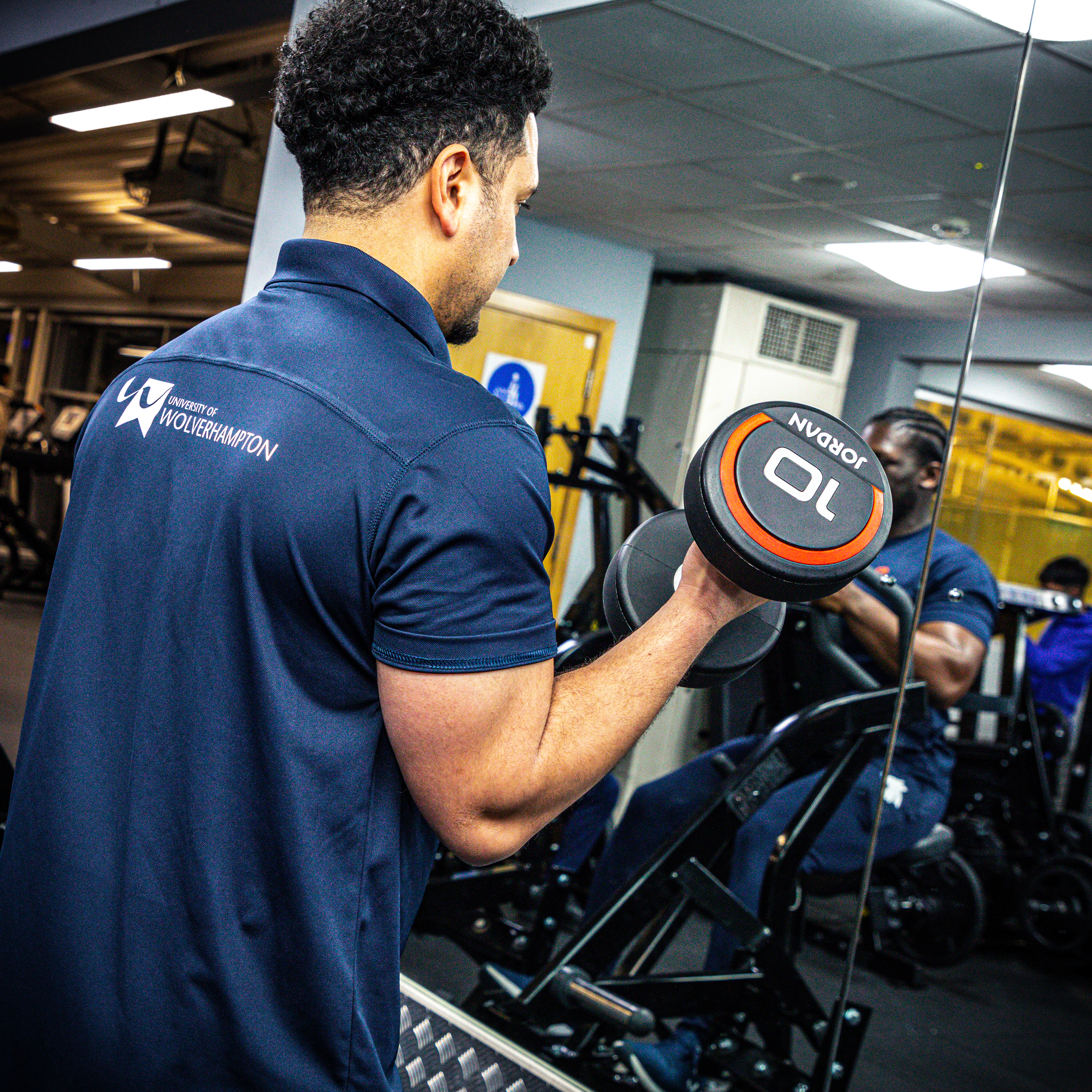 A student in the gym lifting weights, wearing University of Wolverhampton branded sports clothes