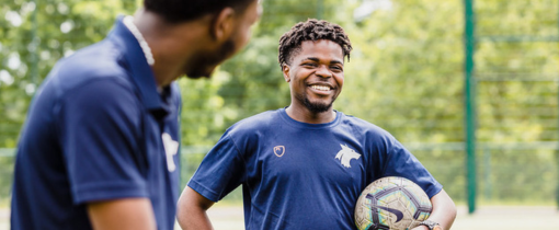 Two students at Walsall Campus in sports uniforms, one holding a football under his arm
