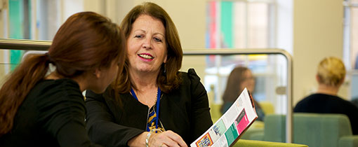 A student being addressed by a member of staff, who is guiding them through a University booklet