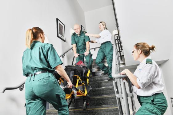 Paramedic students in medical uniforms carrying a stretcher with a mock patient up a set of stairs