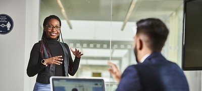 students talking with one at a desk with a laptop while the other stands